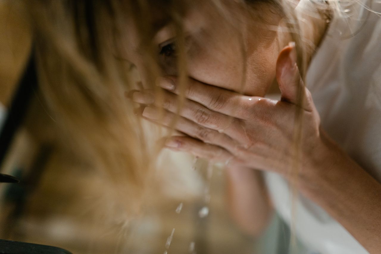 Woman washing her face with water to flush a particle from the eye