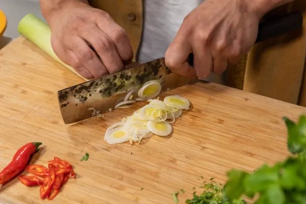 Hands chopping vegetables with a kitchen knife on a cutting board