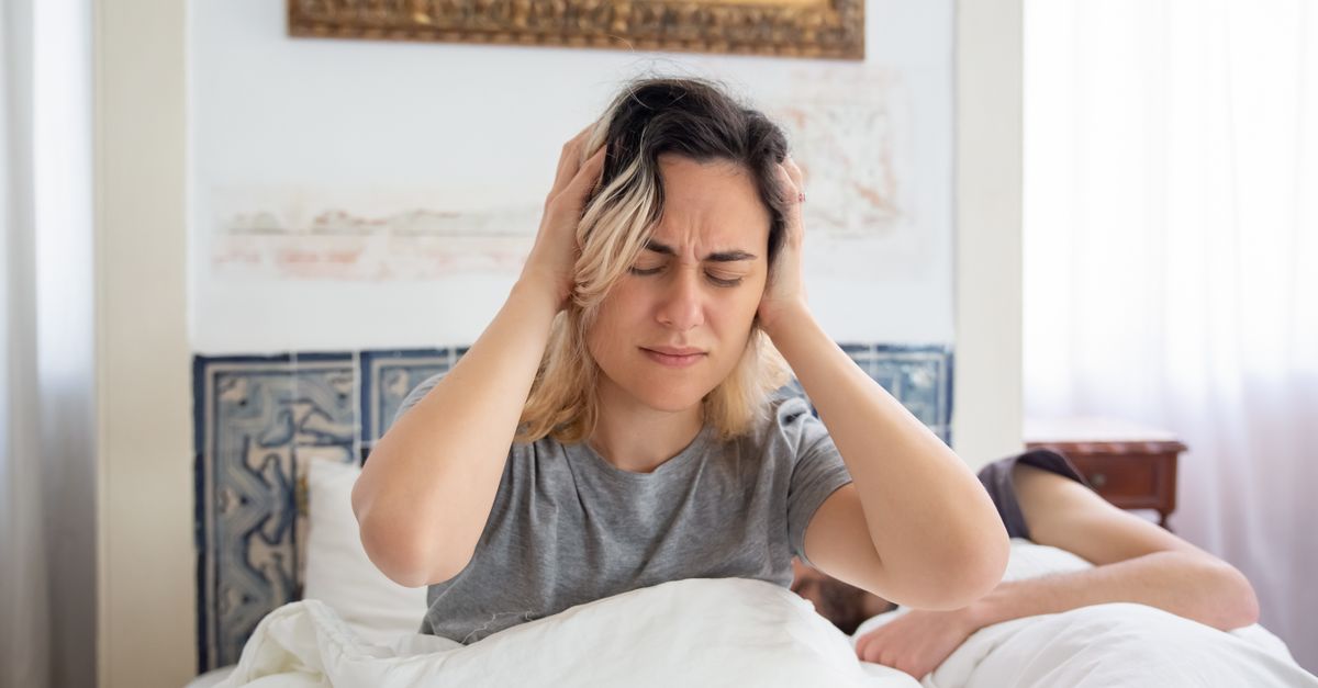 A woman sitting up in bed holding her head, resting after a head bump