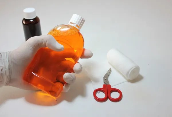 Gloved hand holding an antiseptic bottle next to bandage scissors and gauze