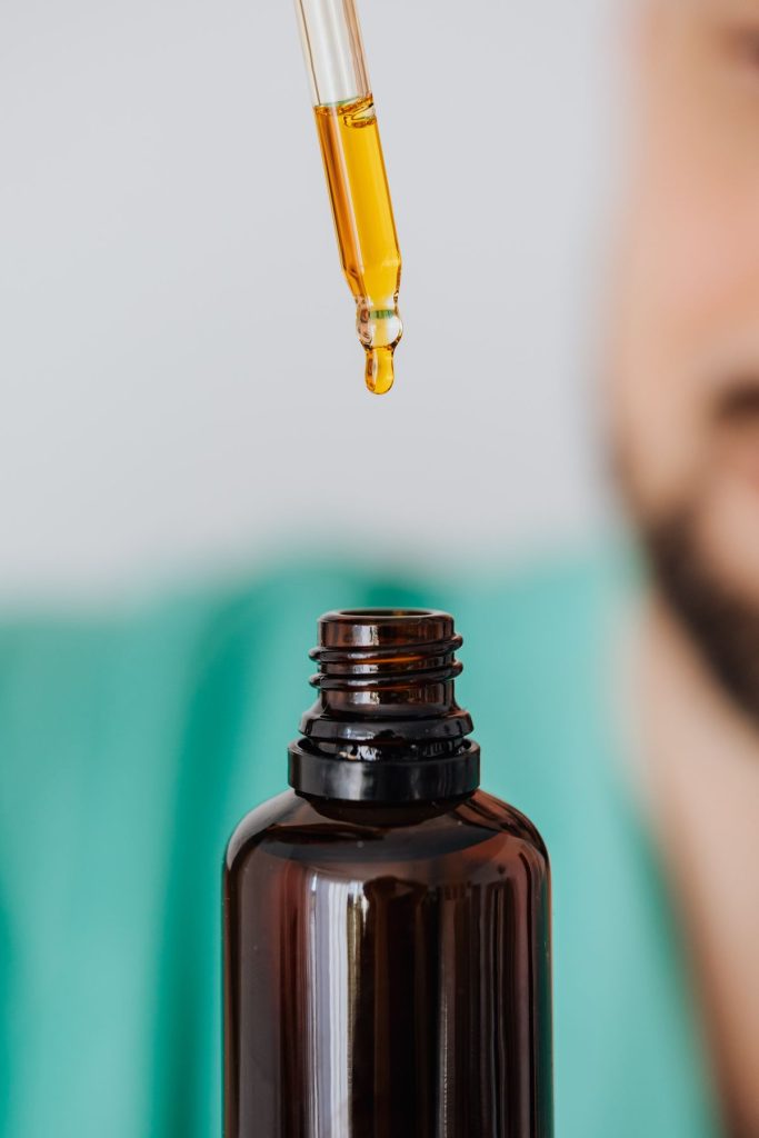 Dropper with golden oil above a small amber bottle